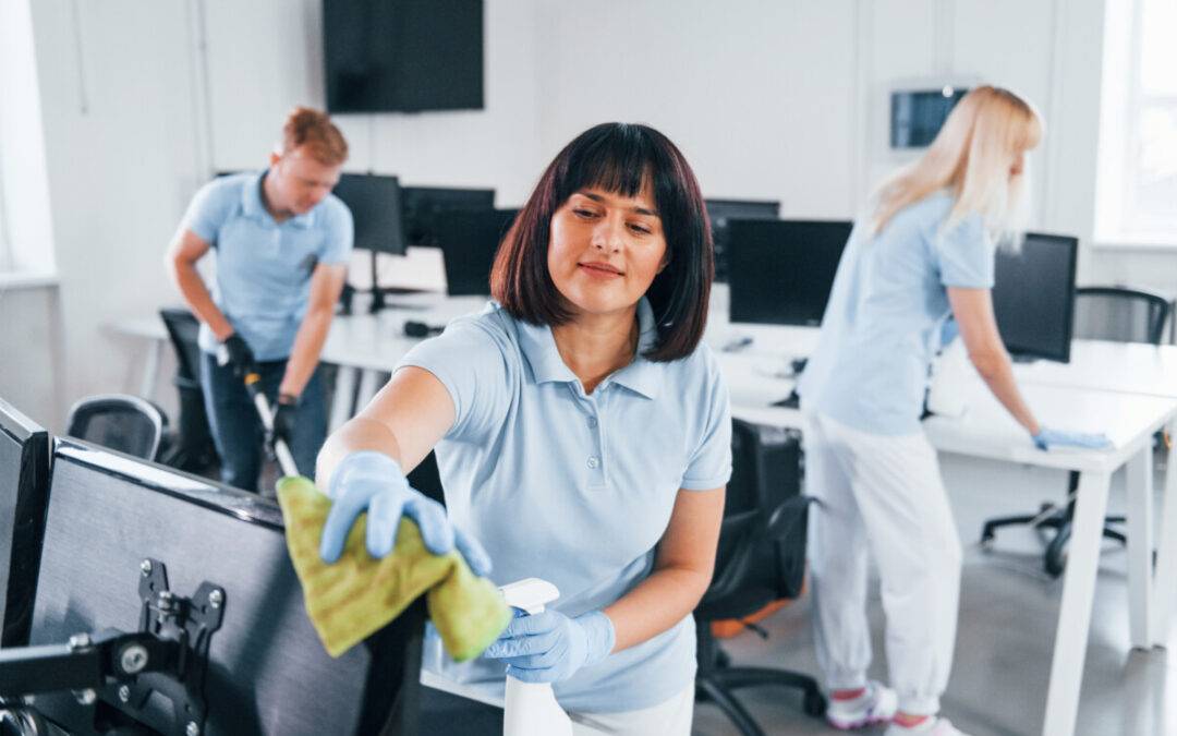 Cleans monitor. Group of workers clean modern office together at daytime